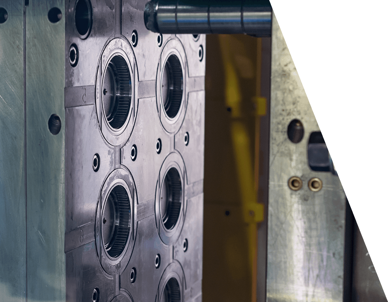 jpeg-optimizer_GettyImages-1407133291 (5) Close-up of a metal industrial mold with multiple circular openings and detailed grooves, positioned near a yellow and silver structure, partially obscured by a black triangular shape on the right.