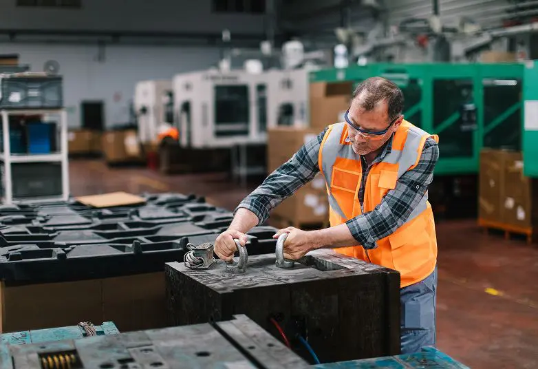 jpeg-optimizer_GettyImages-1507457997 A worker in an orange safety vest inspects industrial equipment in a factory setting.